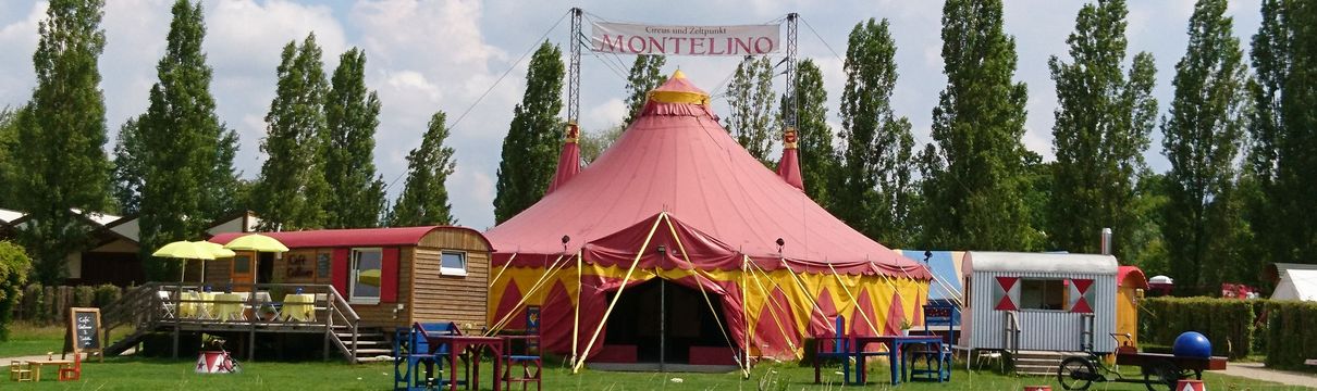 Ein rotes Zirkuszelt auf einer Wiese mit Bäumen im Hintergrund