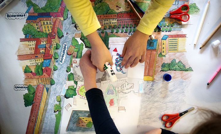 Vier Kinderhände basteln an einem bunten Plan für einen Spielplatz