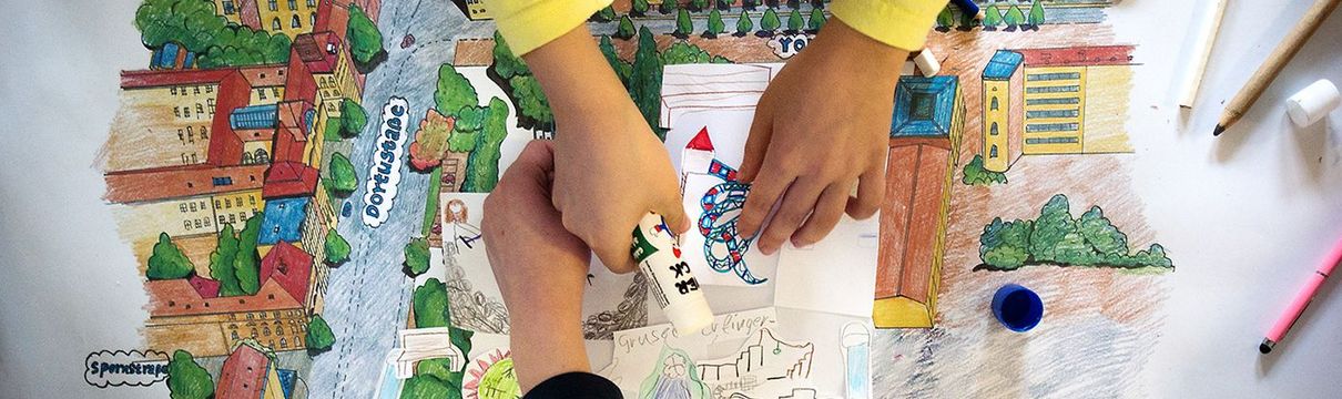 Vier Kinderhände basteln an einem bunten Plan für einen Spielplatz