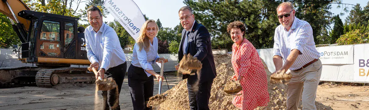 Zwei Frauen und fünf Männer schippen mit Schaufeln Sand für den Spatenstich am Patrizierweg.ich am 