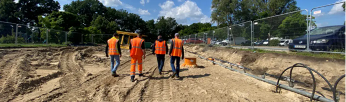 Baustelle mit vier weggehenden Menschen in oragenen Warnwesten.