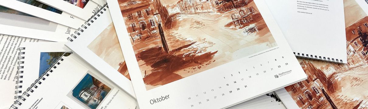 Aufeinanderliegende Exemplare des Kalenders, auf unterschiedlichen Seiten aufgeklappt, liegen übereinander. Im Fokus liegt das Oktober-Motiv.