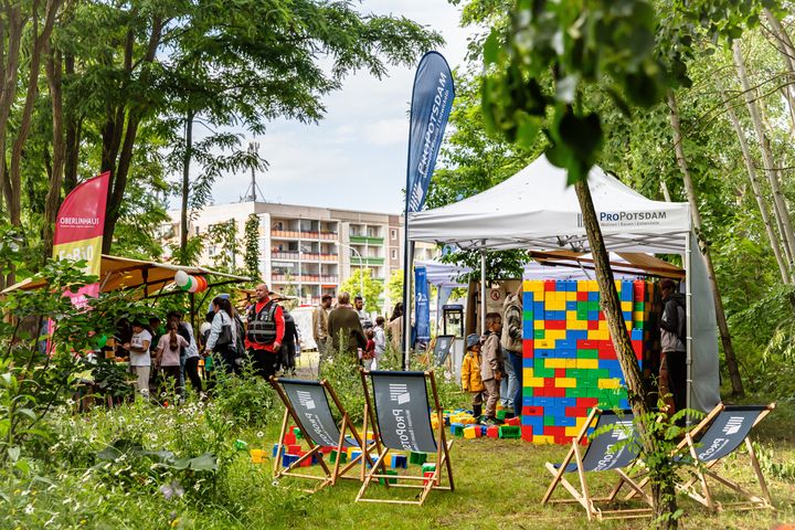 ProPotsdam-Stand beim Gartenstadtfest mit Spielbereich, bunten Bausteinen, Liegestühlen und Personen im Grünen.