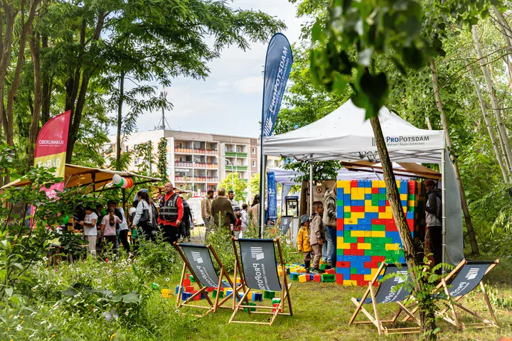 ProPotsdam-Stand beim Gartenstadtfest mit Spielbereich, bunten Bausteinen, Liegestühlen und Personen im Grünen.
