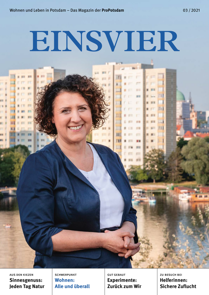 Magazincover der EINSVIER zeigt das Porträt einer lächelnden Frau mit dunklen Locken. Im Hintergrund ist ein Gewässer sichtbar, an welchem mehrere Hochhäuser stehen. 