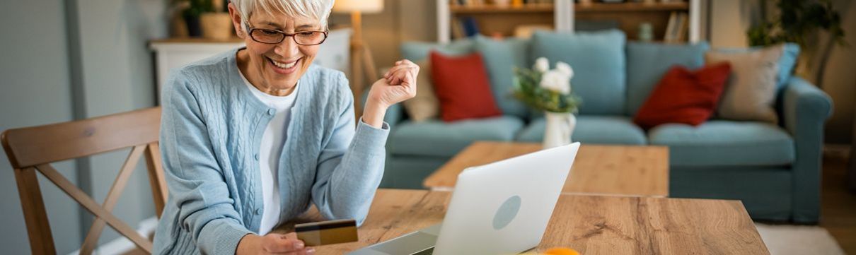 Eine ältere Dame sitzt an einem Tisch und arbeitet an einem Laptop