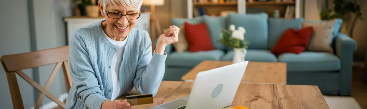Eine ältere Dame sitzt an einem Tisch und arbeitet an einem Laptop