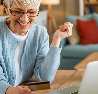 Eine ältere Dame sitzt an einem Tisch und arbeitet an einem Laptop