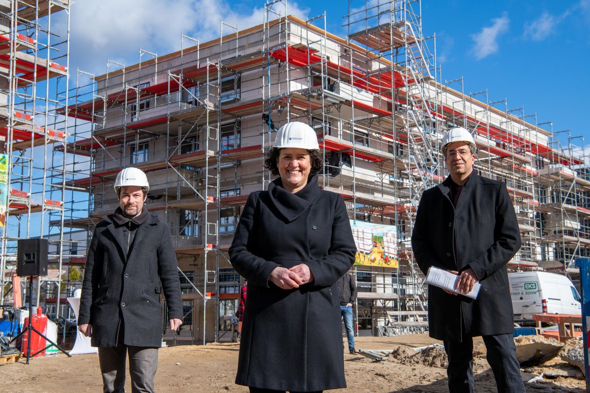 Die Sozialbeigeordnete der Stadt Potsdam, der Geschäftsführer der ProPotsdam und der Fachbereichsleiter Wohnen stehen vor einem mit einem Baugerüst verkleideten Wohngebäude 