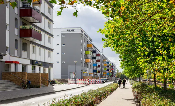 sanierte Plattenbauten mit bunten Balkonen und begrünter Mittelstreifen in der Konrad-Wolf Allee