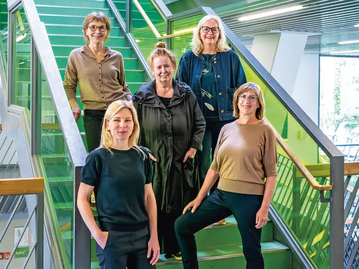 Die Frauen der Gartenstadt Drewitz Fünf Frauen stehen auf einer grünlichen Treppe in einem modernen Gebäude mit großen Fenstern.