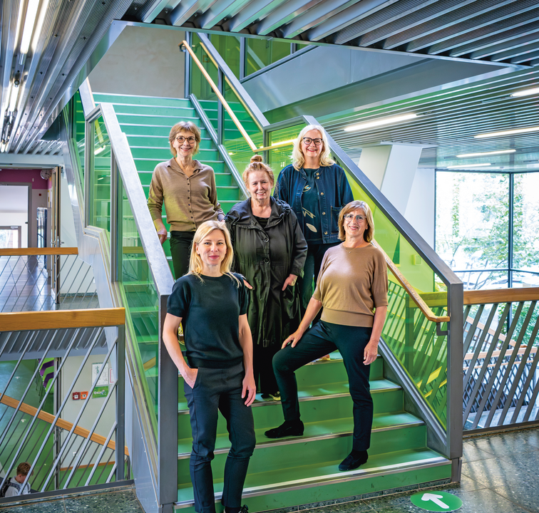 Die Frauen der Gartenstadt Drewitz Fünf Frauen stehen auf einer grünlichen Treppe in einem modernen Gebäude mit großen Fenstern.
