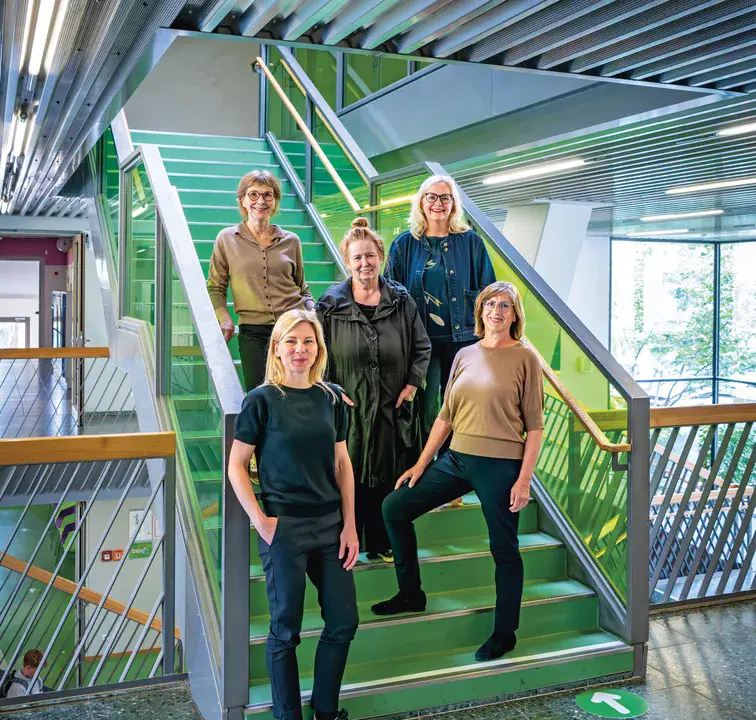 Die Frauen der Gartenstadt Drewitz Fünf Frauen stehen auf einer grünlichen Treppe in einem modernen Gebäude mit großen Fenstern.