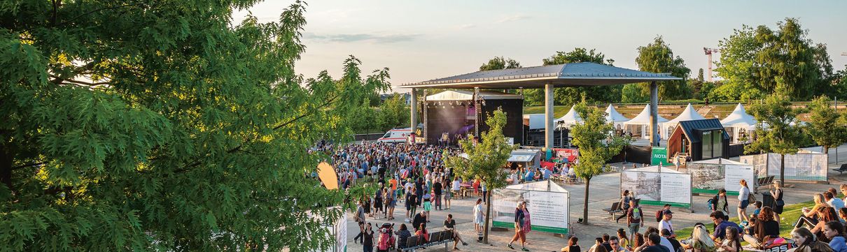 Eine große Menschenmenge steht vor einer Bühne im Volkspark Potsdam. Im Vordergrund sitzen weitere zahlreiche Zuschauer auf der grünen Wiese.