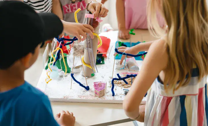 Kinder basteln gemeinsam an einem bunten Modell aus verschiedenen Materialien auf einem Tisch.