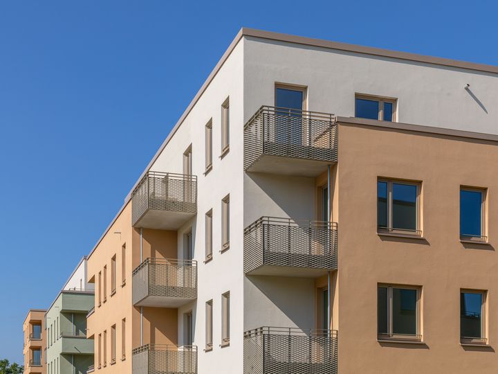 Oberer Gebäudeteil eine weiß-rötlichen Neubaus mit vielen Fenstern und Balkonen