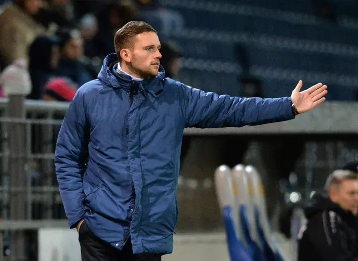 Ein Mann steht auf dem Fußballplatz am Spielfeldrand und gibt den Spielern Handzeichen.