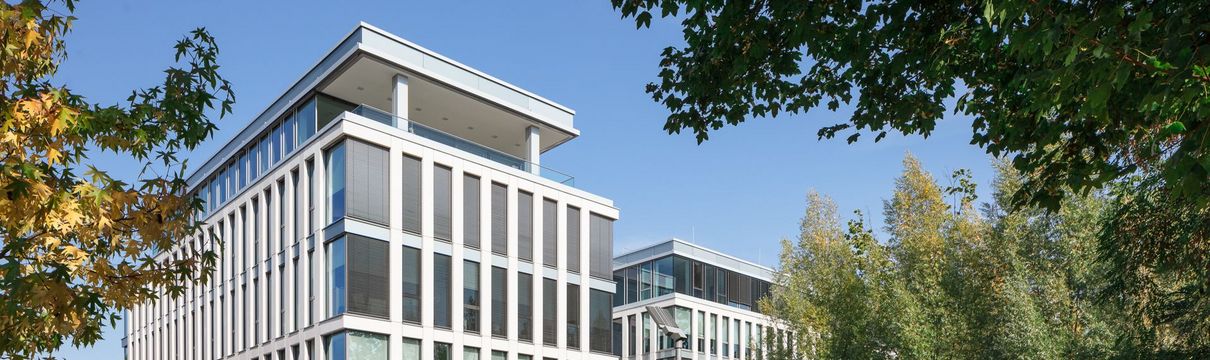 Vierstöckiger, gläserner Firmensitz der ProPotsdam mit Parkmöglichkeiten umgeben von hohen, grünen Bäumen