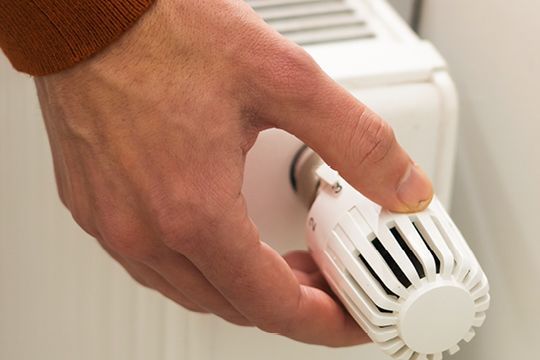 Eine Hand dreht am Thermostat einer Heizung