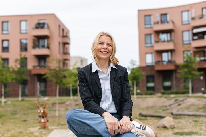 Eine Frau namens Petra Runge sitzt auf einer Bank vor zwei Häusern.