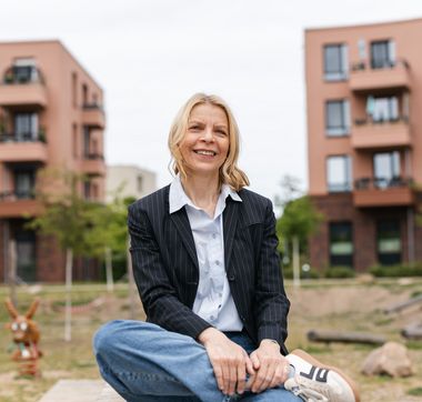 Eine Frau namens Petra Runge sitzt auf einer Bank vor zwei Häusern.
