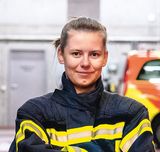 Junge Feuerwehrfrau steht im Innern einer Feuerwehrwache zwischen den Einsatzfahrzeugen