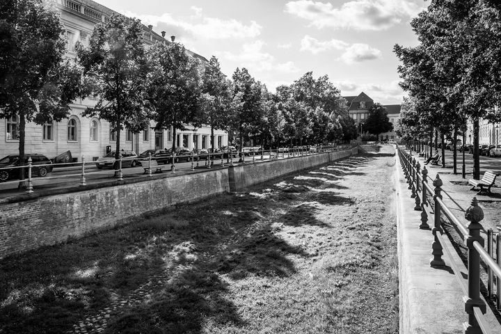 Schwarz-Weiß-Foto eines Stadtkanals ohne Wasser umsäumt von zwei Alleestraßen