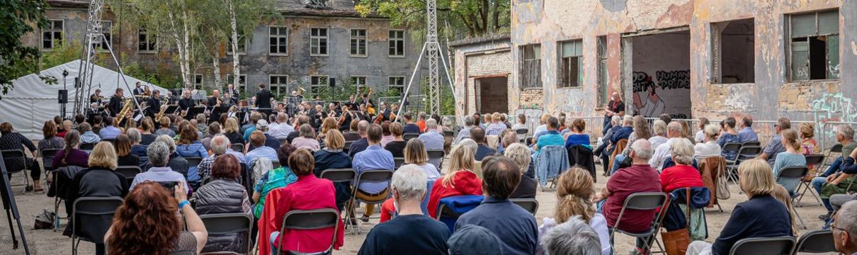 Viele Zuschauer hören ein Konzert von Musikern auf einer Freiluftbühne in Krampnitz.