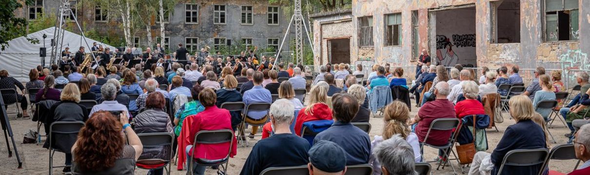 Viele Zuschauer hören ein Konzert von Musikern auf einer Freiluftbühne in Krampnitz.
