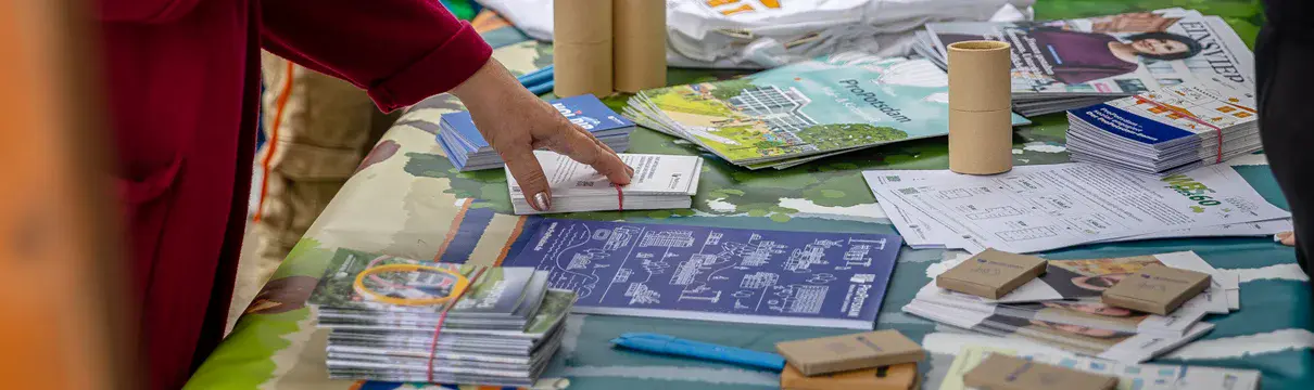 Informationsstand mit Broschüren und Werbematerial bei einer Veranstaltung, Besucher greifen nach Flyern.