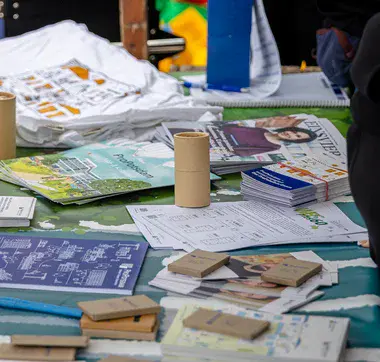 Informationsstand mit Broschüren und Werbematerial bei einer Veranstaltung, Besucher greifen nach Flyern.