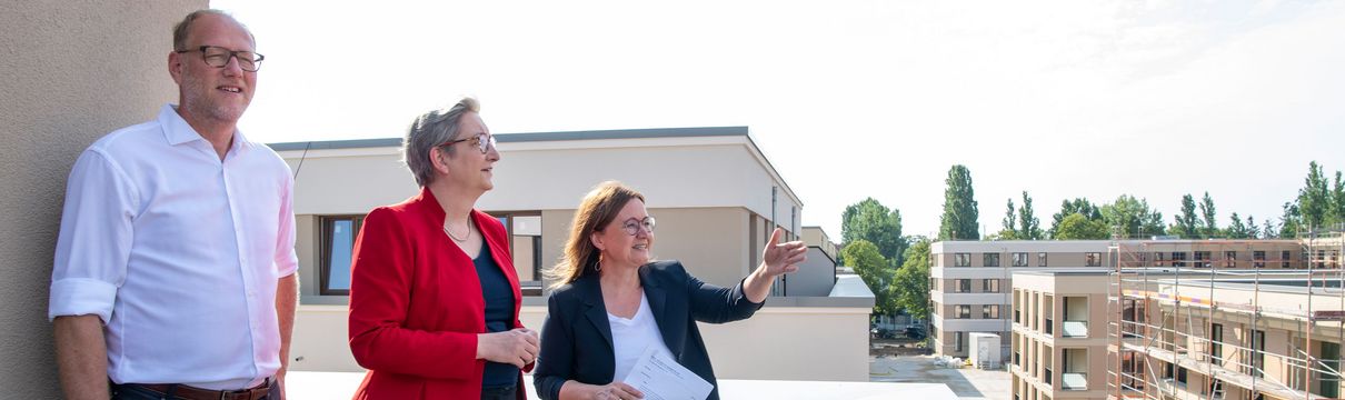 Die Bundesbauministerin, der ProPotsdam-Geschäftsführer und die Bereichsleiterin stehen auf einer Dachterrasse. Davor ist eine Baustelle mit Wohngebäuden zu sehen.