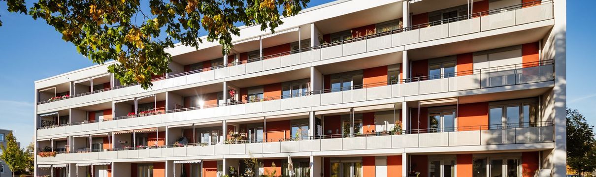 Balkonfassade eines orangen Mehrfamilienhauses mit vielen weißen Balkonen im Sonnenlicht