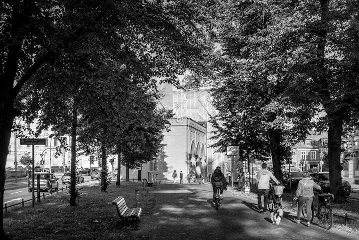 Schwarz-Weiß-Foto einer Fußgängerallee, auf der Radfahrer Richtung eines Baus mit mehreren Torbögen unterwegs sind