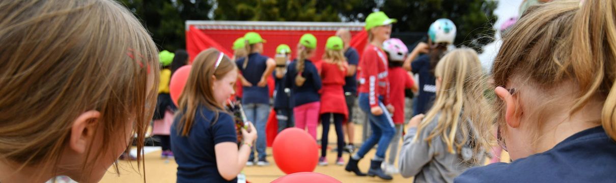 Zwei Mädchen im Schneidersitz sitzen auf dem Boden. Das eine Mädchen hält einen roten Luftballon mit der Aufschrift Sanierungsträger Potsdam in der Hand. Im Hintergrund weitere Kinder.