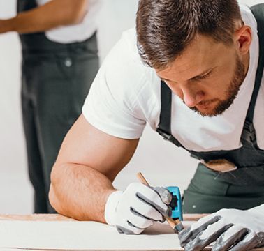 Ein Schreiner markiert auf einer Holzlatte eine Stelle für das Sägen mit einer Stichsäge