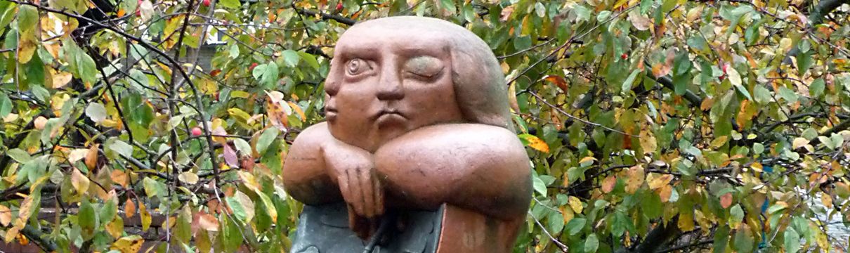 Auf dem Rasen vor einem Baum steht eine Statue.