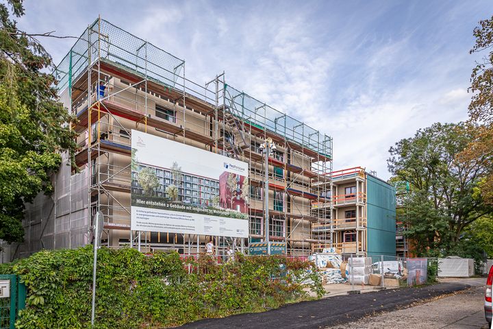 Auf dem Foto ist ein Gebäude mit einem Baugerüst zu sehen. Daran hängt ein Bauschild.