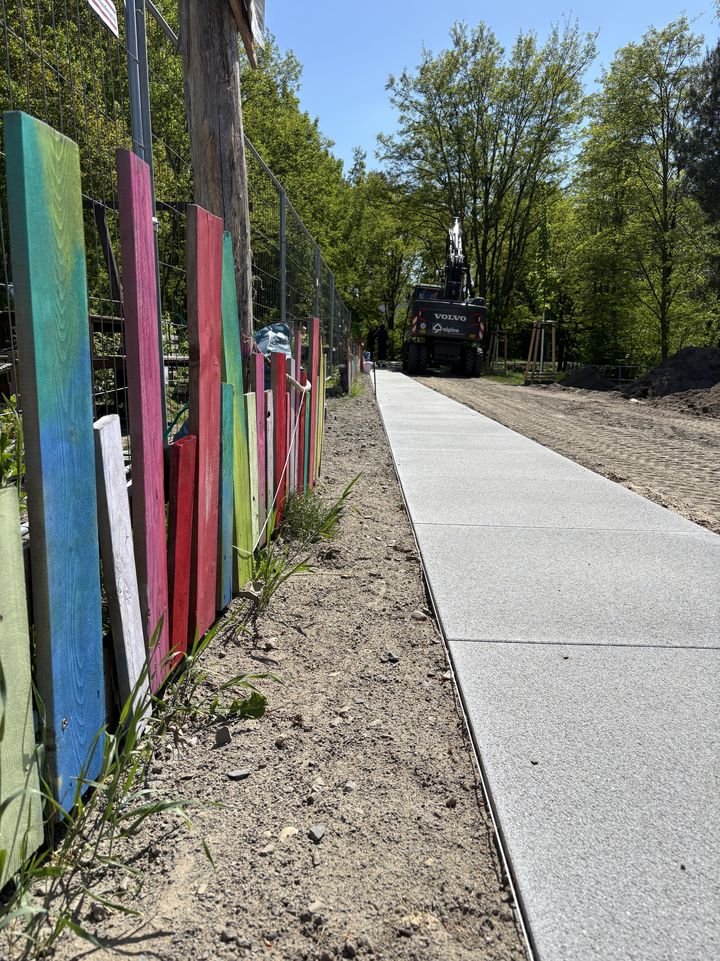Frisch verlegter Gehweg entlang eines bunt bemalten Gartenzauns bei der Wendeschleife in Potsdam-Drewitz. 