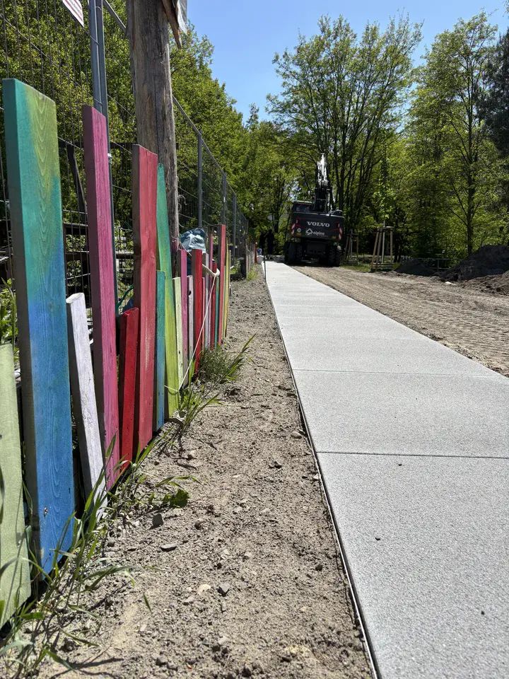 Frisch verlegter Gehweg entlang eines bunt bemalten Gartenzauns bei der Wendeschleife in Potsdam-Drewitz. 