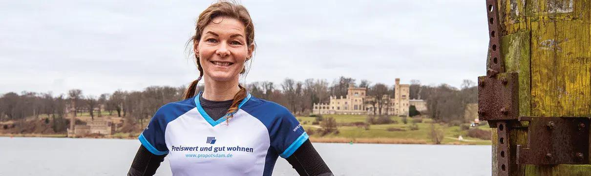 Joggerin steht lächeln vor einer Wasserfläche an deren gegenüberliegender Seite ein Schloss im Hintergrund sichtbar ist