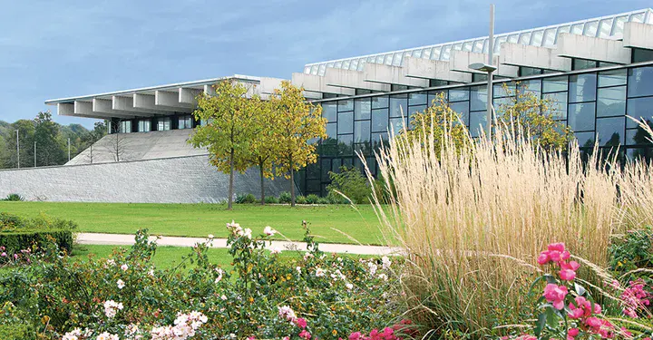 Blumenbeete im Vordergrund Gebäude mit großer Glasfront im Hintergrund