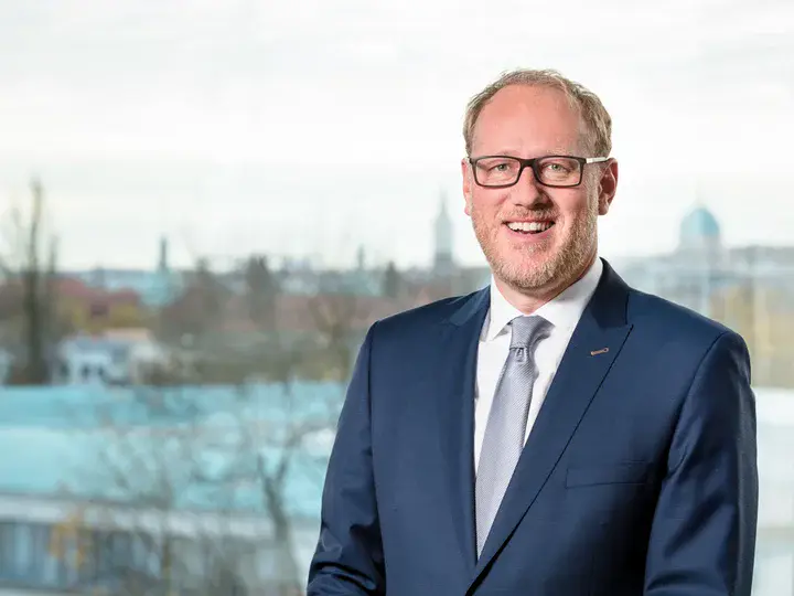 Geschäftsführer der ProPotsdam GmbH, Bert Nicke, steht auf dem Balkon eines höheren Stockwerks lächelnd vor der Stadtkulisse Potsdams