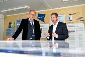 Der Oberbürgermeister der Stadt Potsdam und der Geschätsführer des Entwicklungsträgers Potsdam beugen sich über einen gläsernen Ausstellungstisch und sind im Gespräch.