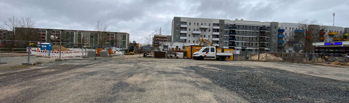 Abgezäunte Baustelle und Baustellenmaterialien. Im Hintergrund sind Geschosswohnungsbauten zu sehen.