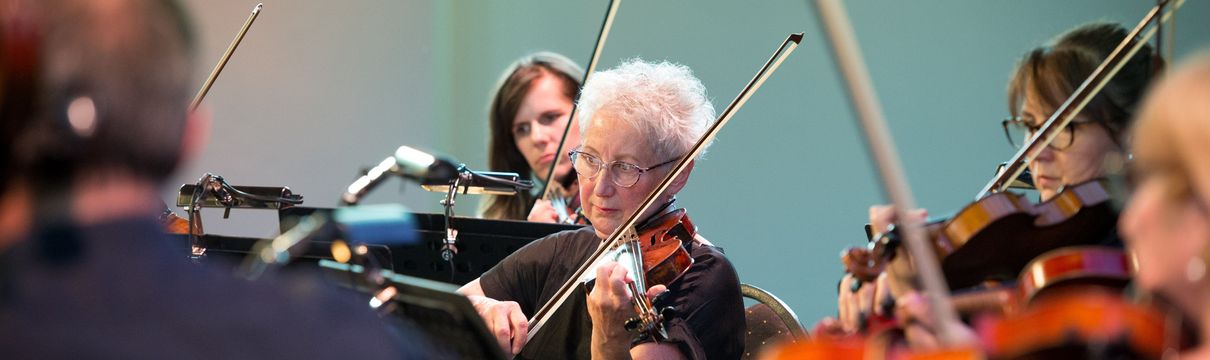 Auschnitt einiger Geigenspielerinnen und-spieler eines Orchesters