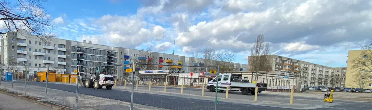 Asphaltierte Straße, Bauzäune und Baustellenfahrzeuge sind zu sehen