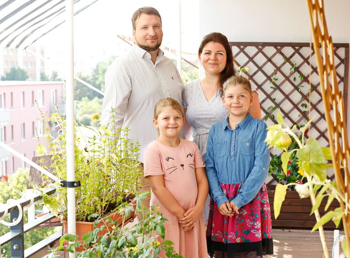 Eine Familie mit zwei Kindern steht auf ihrem Balkon. Es sind Pflanzen und Kräuter zu sehen.  
