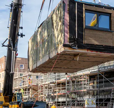 Gebäudeteil, der vor Baustelle mit Hilfe eines Krans in die Luft gehoben wird