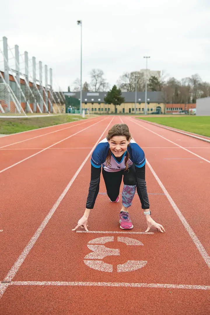 Lächelnde Joggerin befindet sich in Startposition auf einer offiziellen, orangeroten Stadionlaufstrecke